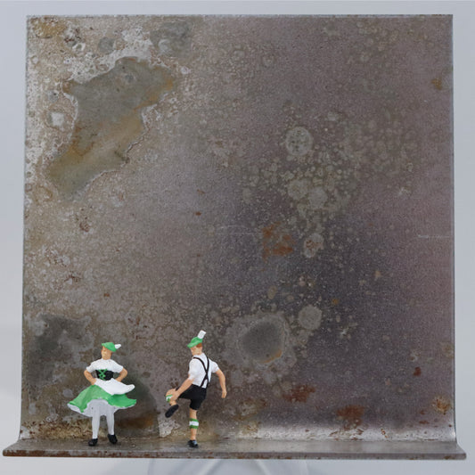 Original Objekt - Assemblage von Katrin Schramm, Titel „Auf der Balz...“ – Metallwinkel mit Miniatur-Figuren: Ein Mann und eine Frau in grün-weißen bayrischen Trachten tanzen auf der linken Seite des Rahmens. Dahinter das Metall des Winkels mit Struktur, als Hintergrund. Objektcollage, erhältlich bei Galerie Waldbach - What The Artist Made