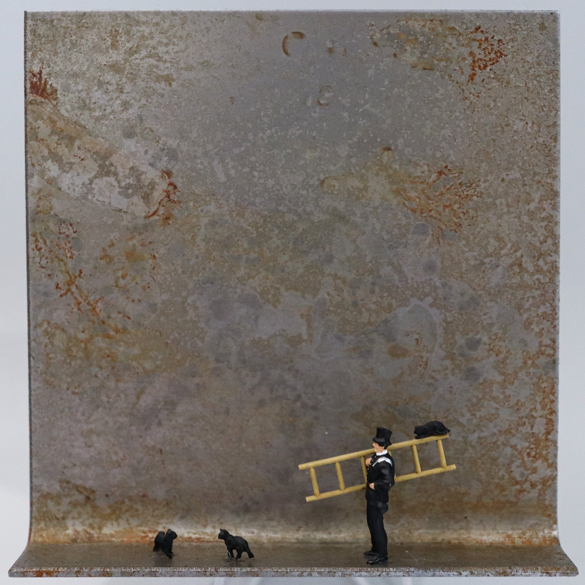 Original Objekt - Assemblage von Katrin Schramm, Titel „Das Glück ist schwarz.“ – Metallwinkel mit Miniatur-Figuren: Ein  Schornsteinfeger mit Leiter steht auf dem Winkel. Auf der Leiter liegt eine schwarze Katze. Zwei weitere stehen am Boden vor dem Schornsteinfeger. Dahinter das Metall des Winkels mit Struktur, als Hintergrund. Objektcollage, erhältlich bei Galerie Waldbach - What The Artist Made