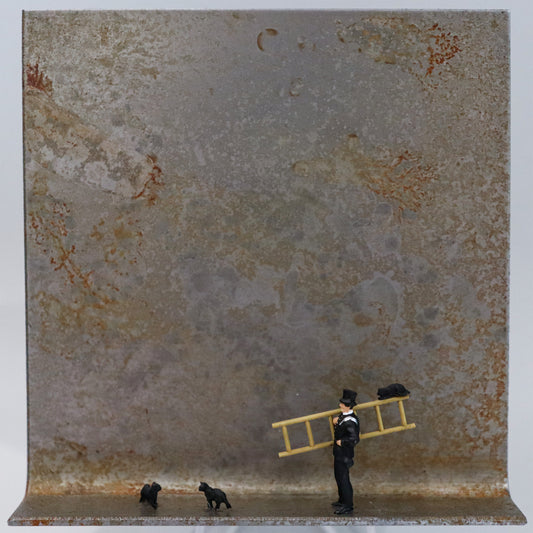Original Objekt - Assemblage von Katrin Schramm, Titel „Das Glück ist schwarz.“ – Metallwinkel mit Miniatur-Figuren: Ein  Schornsteinfeger mit Leiter steht auf dem Winkel. Auf der Leiter liegt eine schwarze Katze. Zwei weitere stehen am Boden vor dem Schornsteinfeger. Dahinter das Metall des Winkels mit Struktur, als Hintergrund. Objektcollage, erhältlich bei Galerie Waldbach - What The Artist Made