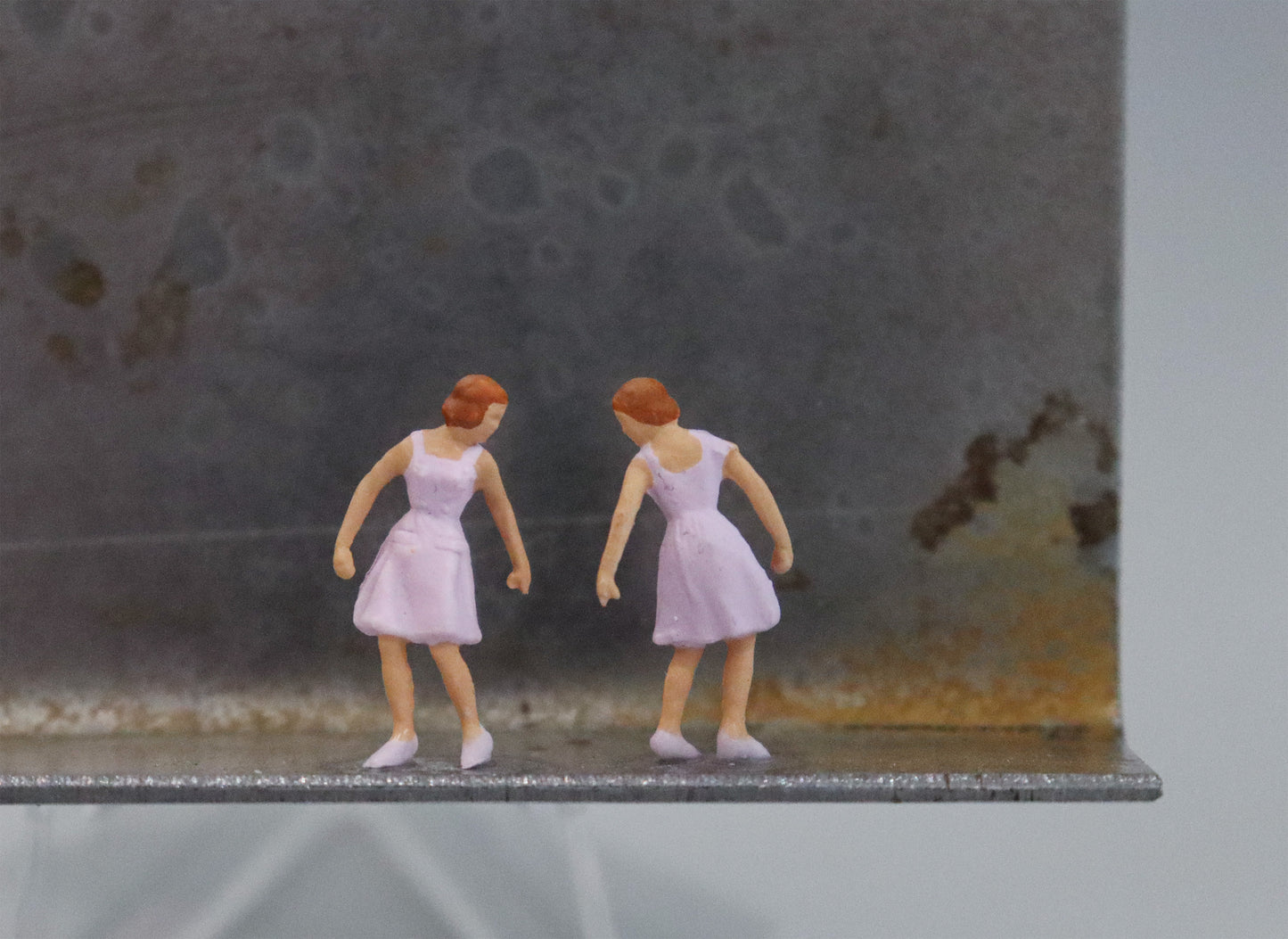 Original Objekt - Assemblage von Katrin Schramm, Titel „Das doppelte Lottchen“ – Metallwinkel mit Miniatur-Figuren, Detailansicht. Dahinter das Metall des Winkels mit Struktur, als Hintergrund. Objektcollage, erhältlich bei Galerie Waldbach - What The Artist Made