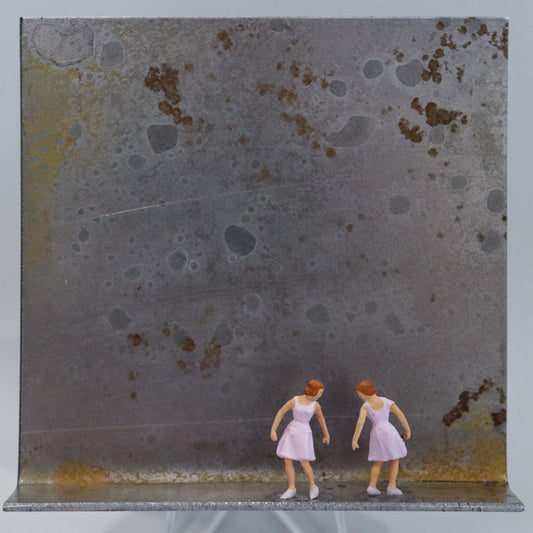 Original Objekt - Assemblage von Katrin Schramm, Titel „Das doppelte Lottchen“ – Metallwinkel mit Miniatur-Figuren: Zwei Mädchen/junge Frauen in rosa Kleidern stehen sich in derselben Haltung gegenüber und sehen gleich aus. Dahinter das Metall des Winkels mit Struktur, als Hintergrund. Objektcollage, erhältlich bei Galerie Waldbach - What The Artist Made