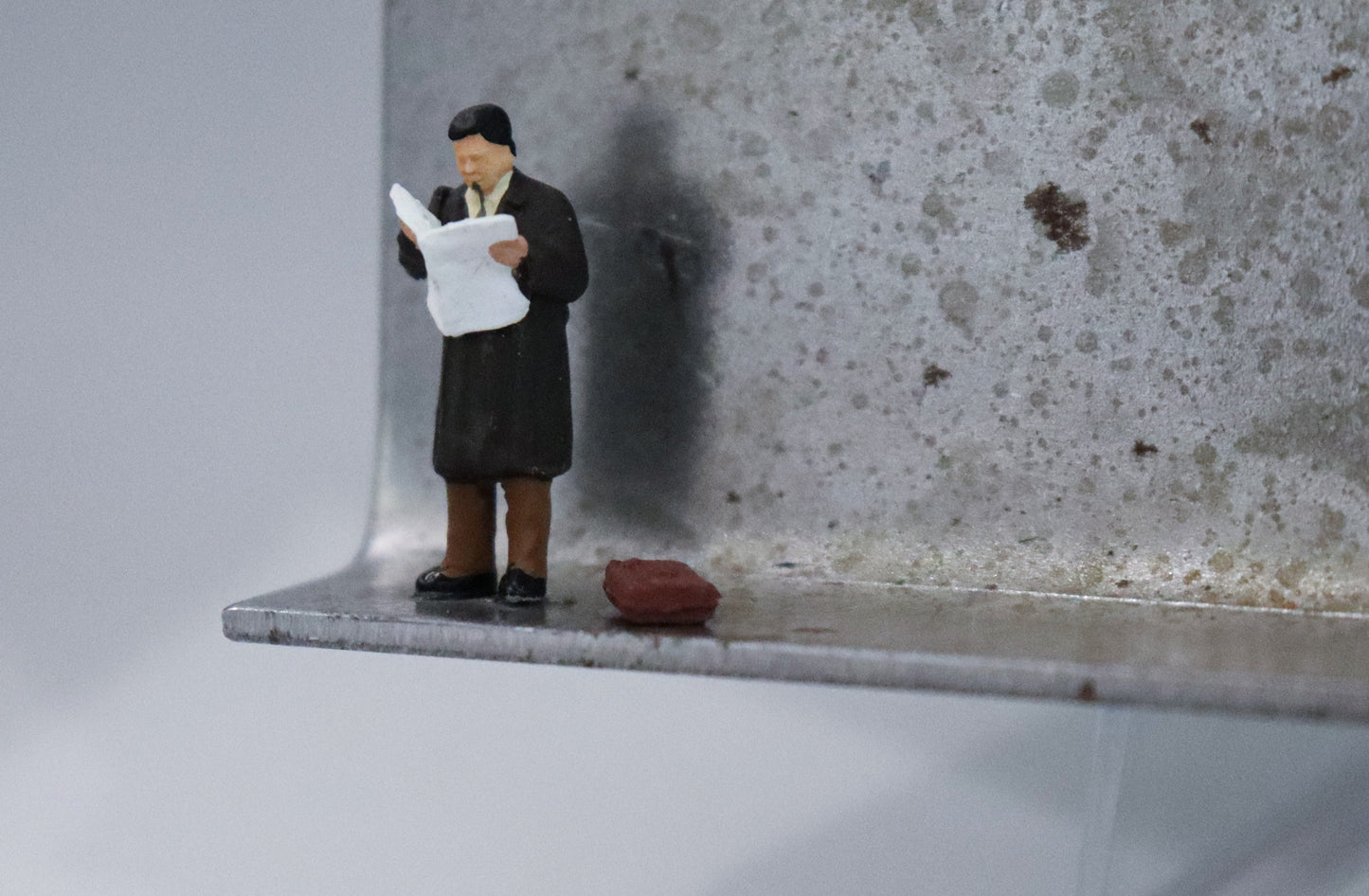 Original Objekt - Assemblage von Katrin Schramm, Titel „Der letzte Zeitungsleser?“ – Metallwinkel mit Miniatur-Figur, Detailansicht. Objektcollage, erhältlich bei Galerie Waldbach - What The Artist Made