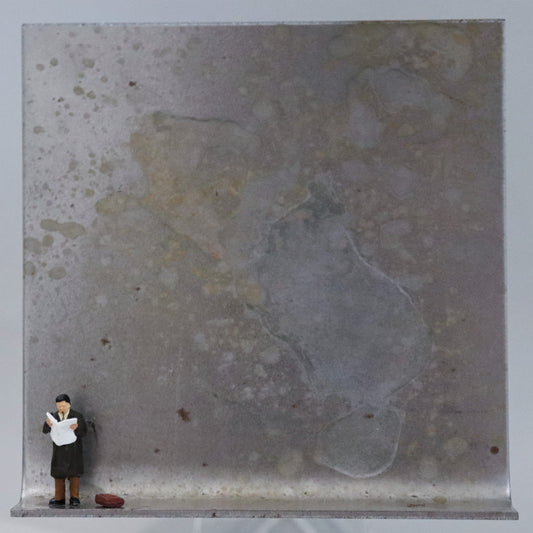 Original Objekt - Assemblage von Katrin Schramm, Titel „Der letzte Zeitungsleser?“ – Metallwinkel mit Miniatur-Figur: Ein Mann steht am linken Rand des Winkels und liest in einer aufgeschlagenen Zeitung. Neben ihm liegt  seine Tasche. Dahinter das Metall des Winkels mit Struktur, als Hintergrund. Objektcollage, erhältlich bei Galerie Waldbach - What The Artist Made