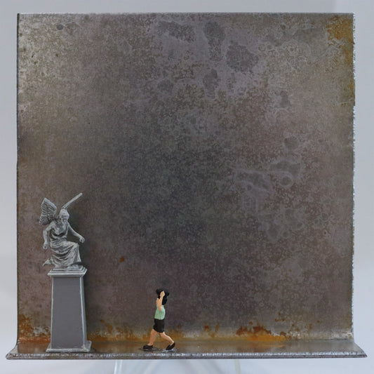 Original Objekt - Assemblage von Katrin Schramm, Titel „Alle haben einen verdient“  – Metallwinkel mit Miniatur-Figuren: Am linken Rand des Winkels steht eine Engelsfigur auf einem hohen Podest. Neben ihr läuft ein Kind, dass einen Gegenstand über dem Kopf trägt, auf die Statue zu. Dahinter das Metall des Winkels mit Struktur, als Hintergrund. Objektcollage, erhältlich bei Galerie Waldbach - What The Artist Made