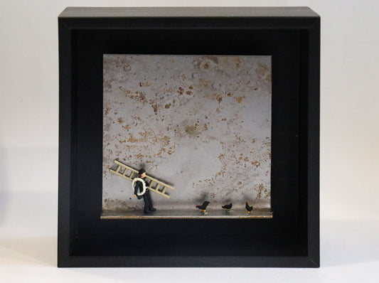 Original Objekt - Assemblage von Katrin Schramm, Titel „Das Glück ist schwarz“ – Metallwinkel mit Miniatur-Figuren: Ein Schornsteinfeger steht mit Leiter und Seil steht am linken Rand des Winkels. Rechts von ihm drei schwarze Hühner. Dahinter das Metall des Winkels mit Struktur, als Hintergrund. In einem schwarzen Rahmen aus Holz. Objektcollage, erhältlich bei Galerie Waldbach - What The Artist Made