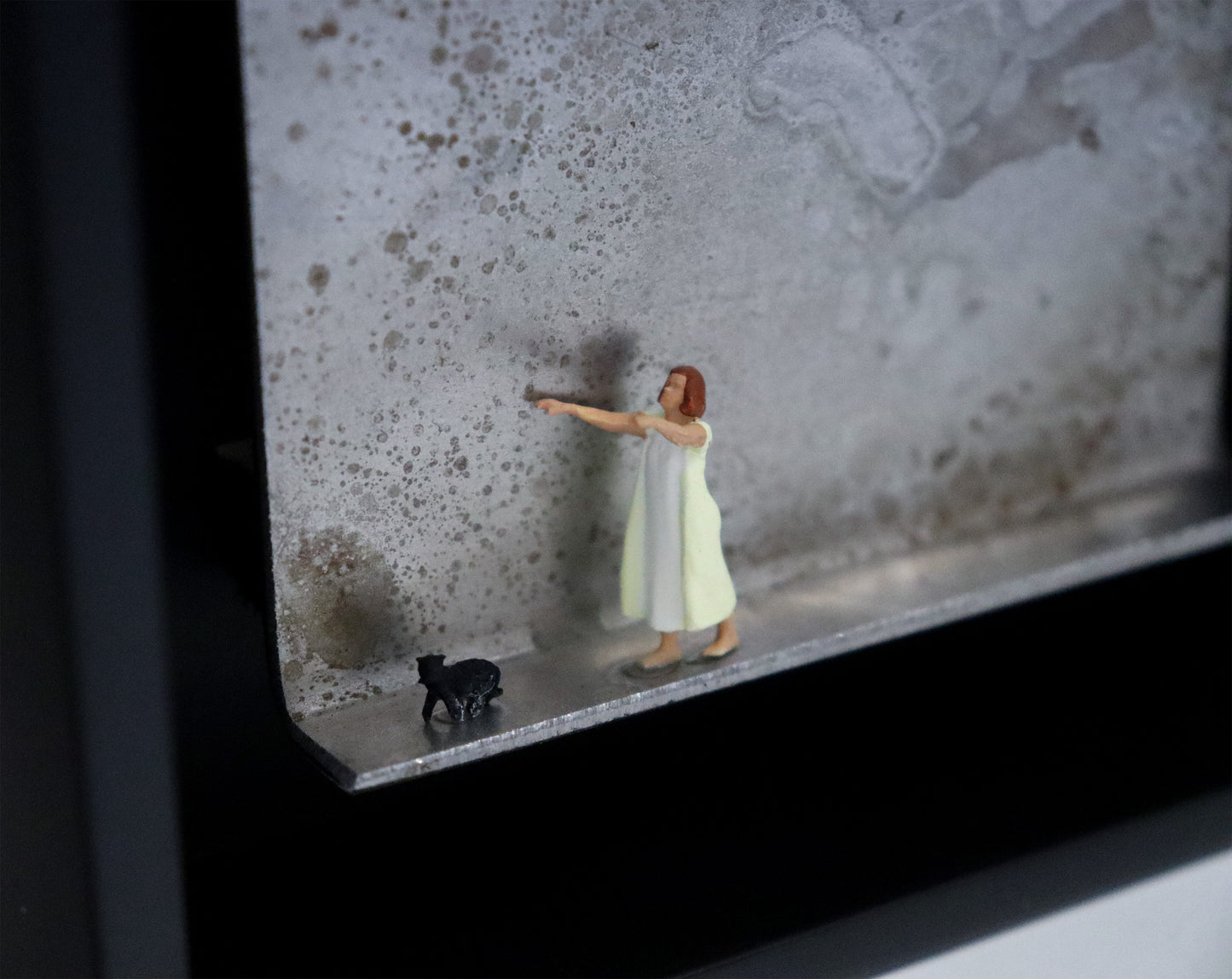 Original Objekt - Assemblage von Katrin Schramm, Titel „Ein schmaler Grat.“ – Metallwinkel mit Miniatur-Figuren, Detailansicht. Dahinter das Metall des Winkels mit Struktur, als Hintergrund. Objektcollage im schwarzen Rahmen, erhältlich bei Galerie Waldbach - What The Artist Made