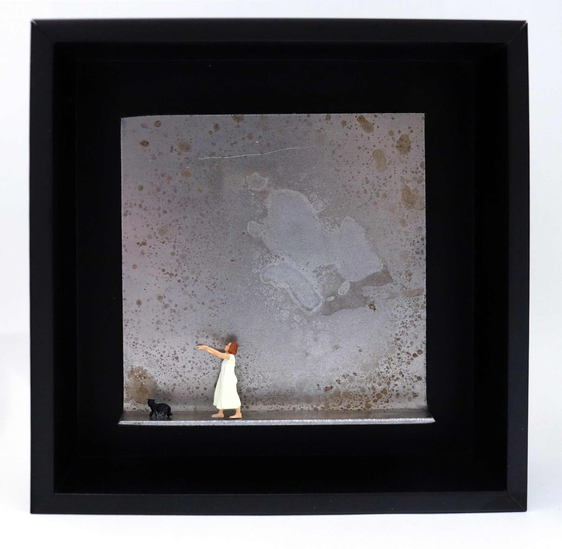 Original Objekt - Assemblage von Katrin Schramm, Titel „Ein schmaler Grat.“ – Metallwinkel mit Miniatur-Figuren: Eine Frau im Nachthemd läuft schlafwandelnd, die Arme ausgestreckt, auf den linken Rand zu.  Vor ihr läuft eine schwarze Katze in die gleiche Richtung. Dahinter das Metall des Winkels mit Struktur, als Hintergrund. Objektcollage im schwarzen Rahmen, erhältlich bei Galerie Waldbach - What The Artist Made