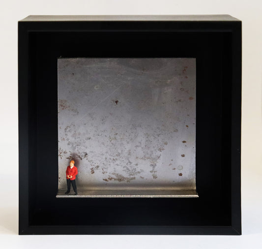 Original Objekt - Assemblage von Katrin Schramm, Titel „Geschafft“ – Metallwinkel mit Miniatur-Figur: Eine Person, dem Erscheinen nach soll sie Angela Merkel darstellen, steht am linken Rand des Winkels. Sie trägt einen roten Blazer und  hat die Hände zur typischen Raute geformt. Dahinter das Metall des Winkels mit Struktur, als Hintergrund. In einem schwarzen Rahmen aus Holz. Objektcollage, erhältlich bei Galerie Waldbach - What The Artist Made