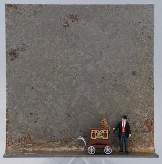 Original Objekt - Assemblage von Katrin Schramm, Titel „Gib dem Affen Zucker...“ – Metallwinkel mit Miniatur-Figuren: Ein Mann steht neben seiner Drehorgel. Auf der Drehorgel sitzt ein Affe, der die Hand aufhält. Dahinter das Metall des Winkels mit Struktur, als Hintergrund. Objektcollage, erhältlich bei Galerie Waldbach - What The Artist Made