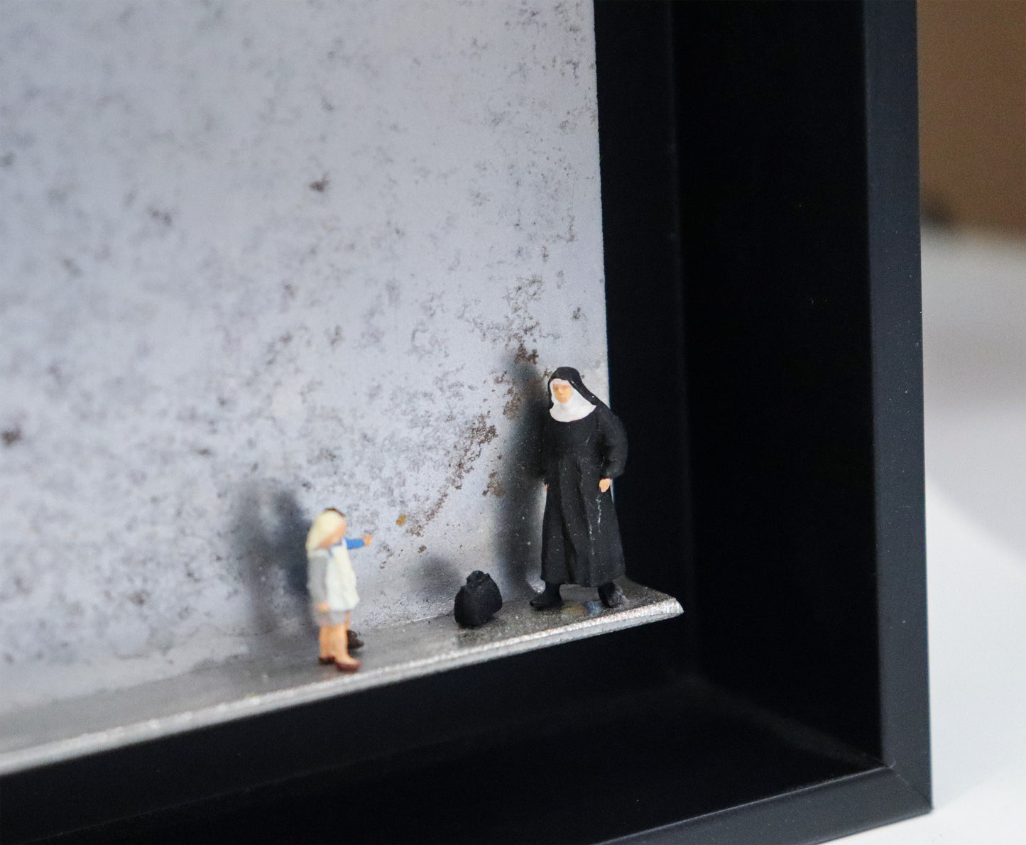 Original Objekt - Assemblage von Katrin Schramm, Titel „Jedes Kind ist kostbar.“ – Metallwinkel mit Miniatur-Figuren, Detailansicht. Objektcollage im schwarzen Rahmen, erhältlich bei Galerie Waldbach - What The Artist Made