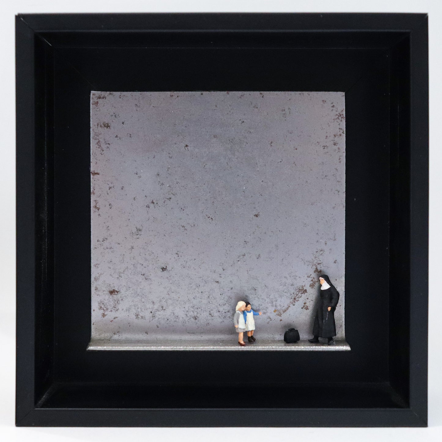 Original Objekt - Assemblage von Katrin Schramm, Titel „Jedes Kind ist kostbar.“ – Metallwinkel mit Miniatur-Figuren: Eine Nonne steht am rechten Rand des Winkels. Vor  ihr eine schwarze Reisetasche. Davor stehen zwei Kinder, ihr zugewandt. Dahinter das Metall des Winkels mit Struktur, als Hintergrund. Objektcollage im schwarzen Rahmen, erhältlich bei Galerie Waldbach - What The Artist Made