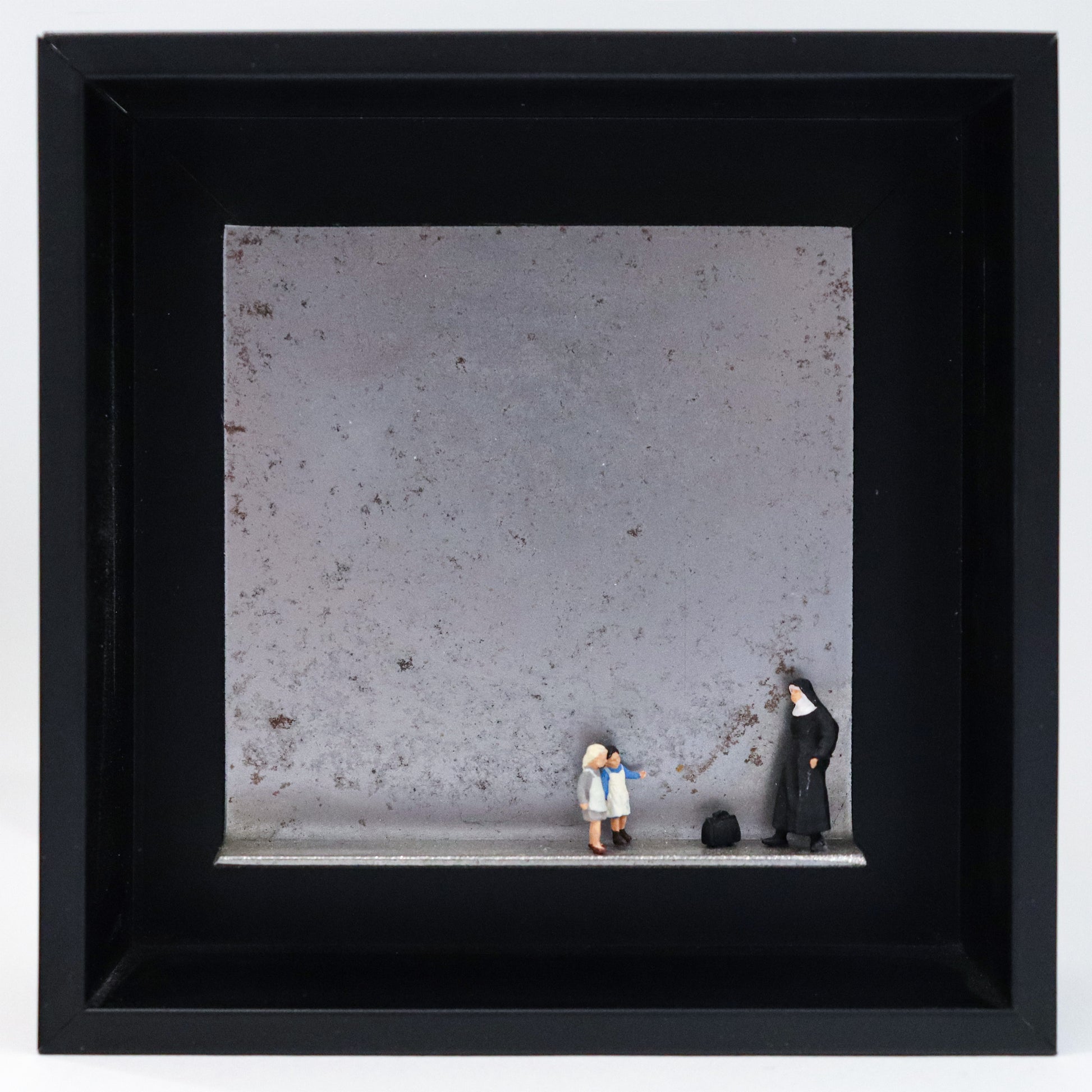 Original Objekt - Assemblage von Katrin Schramm, Titel „Jedes Kind ist kostbar.“ – Metallwinkel mit Miniatur-Figuren: Eine Nonne steht am rechten Rand des Winkels. Vor  ihr eine schwarze Reisetasche. Davor stehen zwei Kinder, ihr zugewandt. Dahinter das Metall des Winkels mit Struktur, als Hintergrund. Objektcollage im schwarzen Rahmen, erhältlich bei Galerie Waldbach - What The Artist Made