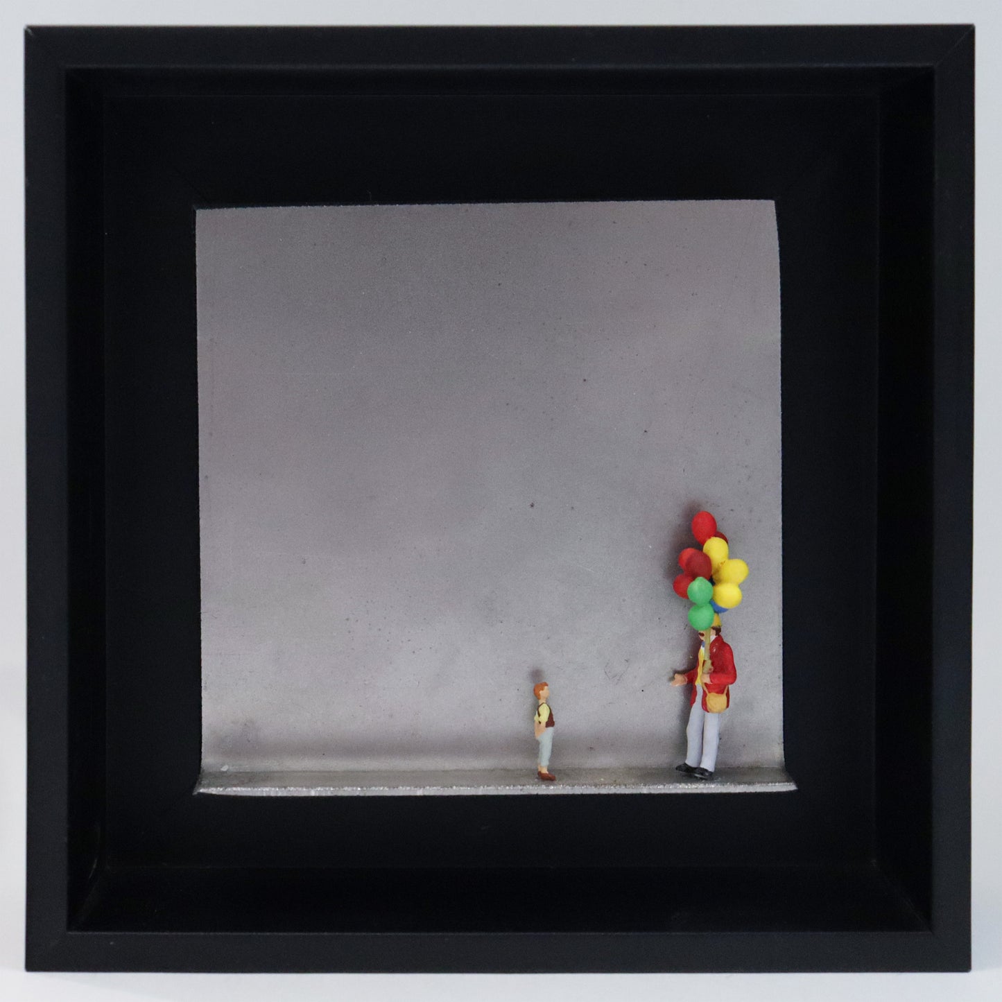 Original Objekt - Assemblage von Katrin Schramm, Titel „Lass sie fliegen...“ – Metallwinkel mit Miniatur-Figuren: Ein Ballonverkäufer steht auf der rechten Seite des Winkels und hält ein Bündel Ballons in der Hand. Vor ihm steht ein Kind und schaut  zu ihm und den Ballons hoch. Dahinter das Metall des Winkels mit Struktur, als Hintergrund. Objektcollage im schwarzen Rahmen, erhältlich bei Galerie Waldbach - What The Artist Made