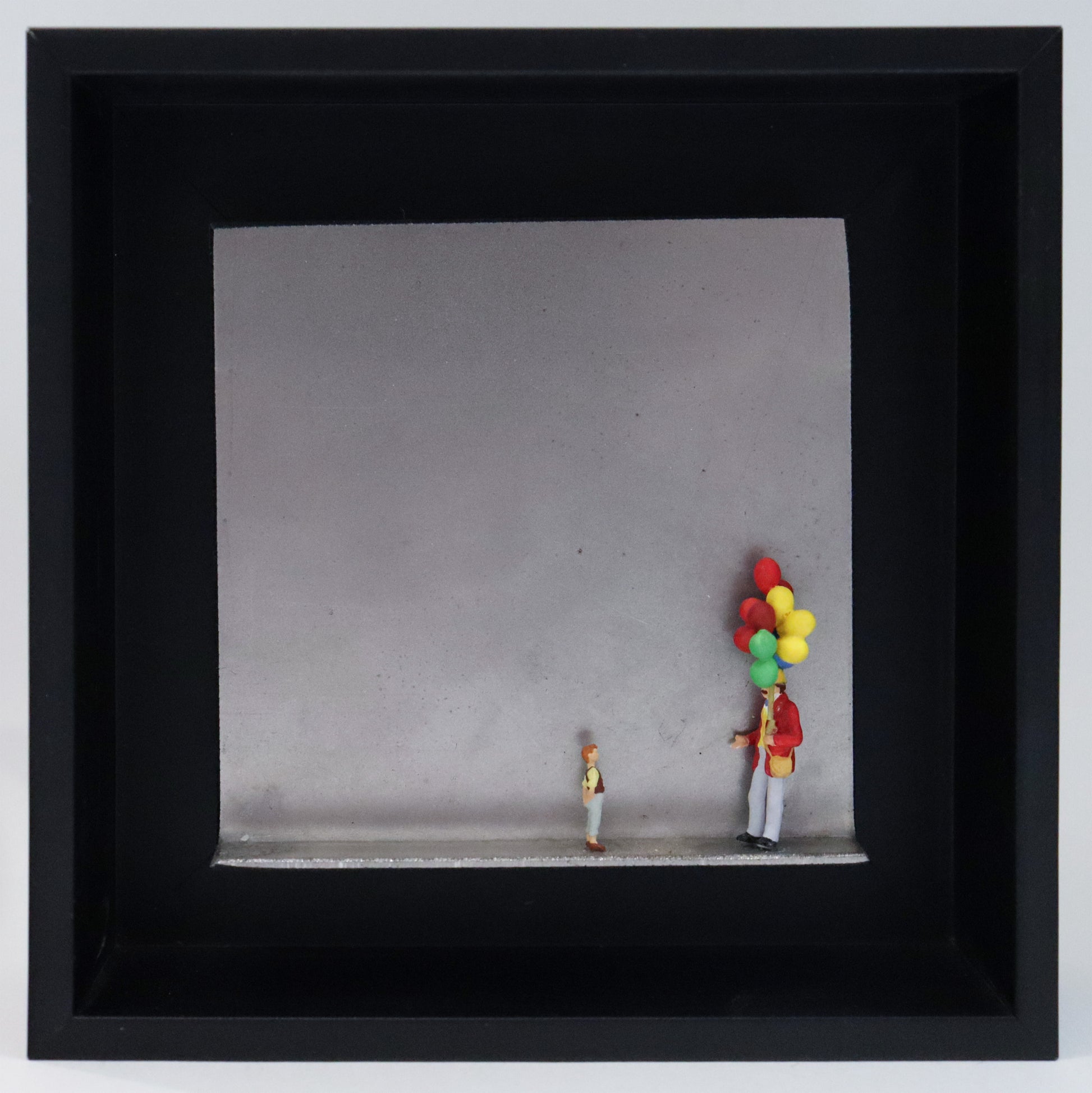 Original Objekt - Assemblage von Katrin Schramm, Titel „Lass sie fliegen...“ – Metallwinkel mit Miniatur-Figuren: Ein Ballonverkäufer steht auf der rechten Seite des Winkels und hält ein Bündel Ballons in der Hand. Vor ihm steht ein Kind und schaut  zu ihm und den Ballons hoch. Dahinter das Metall des Winkels mit Struktur, als Hintergrund. Objektcollage im schwarzen Rahmen, erhältlich bei Galerie Waldbach - What The Artist Made