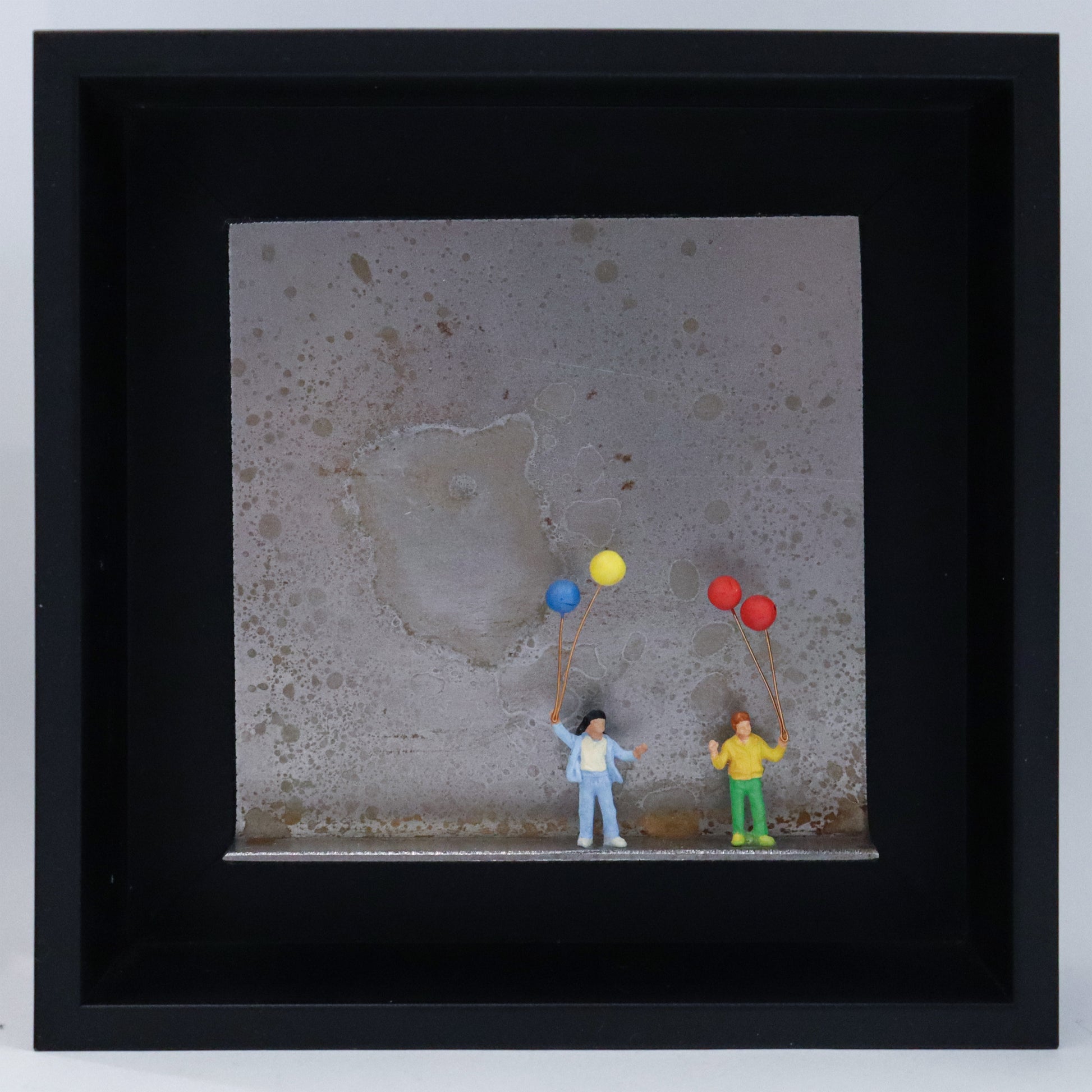 Original Objekt - Assemblage von Katrin Schramm, Titel „Mehr als nur Luft...“ – Metallwinkel mit Miniatur-Figuren: Zwei Kinder stehen auf dem Boden des Winkels und halten jeweils zwei Luftballons in der Hand. Dahinter das Metall des Winkels mit Struktur, als Hintergrund. Objektcollage im schwarzen Rahmen, erhältlich bei Galerie Waldbach - What The Artist Made