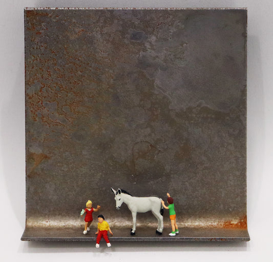 Original Objekt - Assemblage von Katrin Schramm, Titel „Mit Eselsgeduld...“ – Metallwinkel mit Miniatur-Figuren: Mittig stehend/sitzend zwei Kinder, daneben ein weißer Esel, rechts hinter diesem ein weiteres Kind stehend, vermeintlich den Esel schiebend. Dahinter das Metall des Winkels mit Struktur, als Hintergrund. - Objektcollage, erhältlich bei Galerie Waldbach - What The Artist Made