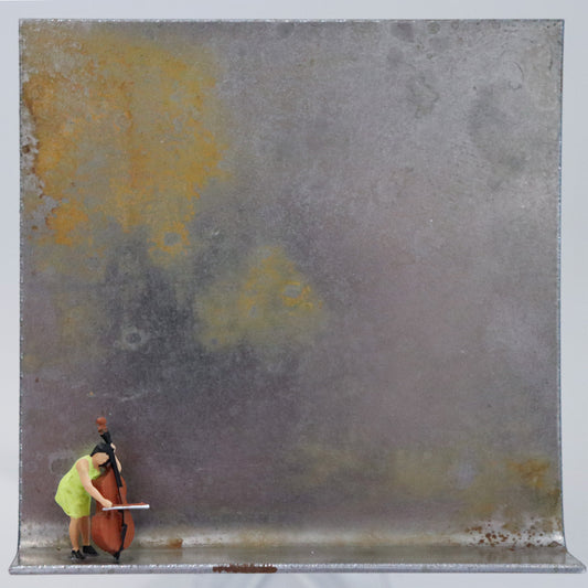 Original Objekt - Assemblage von Katrin Schramm, Titel „Schwer zu tragen. leicht zu  lieben.“  – Metallwinkel mit Miniatur-Figur: Eine Frau im gelben Kleid steht mit einem Kontrabass am linken Rand des Winkels und spielt auf dem Instrument. Dahinter das Metall des Winkels mit Struktur, als Hintergrund. Objektcollage, erhältlich bei Galerie Waldbach - What The Artist Made