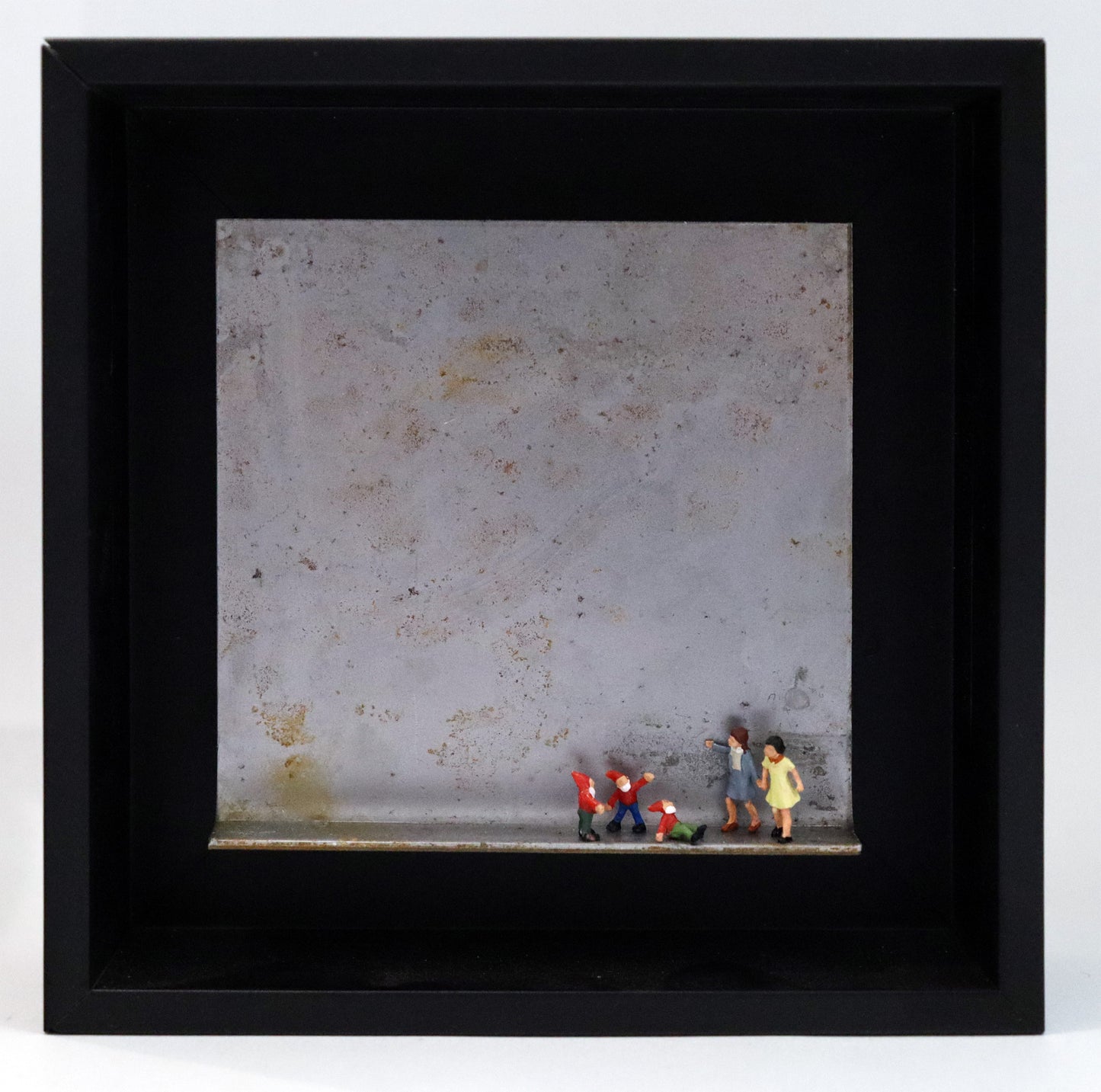 Original Objekt - Assemblage von Katrin Schramm, Titel „Zwergengeflüster.“ – Metallwinkel mit Miniatur-Figuren: Zwei Frauen/Mädchen stehen am rechten Rand des Winkels. Neben ihnen eine Gruppe aus drei Zwergen mit roten Mützen. Einer sitzt und schaut zu ihnen hoch, die beiden anderen stehen dahinter. Dahinter das Metall des Winkels mit Struktur, als Hintergrund. Objektcollage im schwarzen Rahmen, erhältlich bei Galerie Waldbach - What The Artist Made