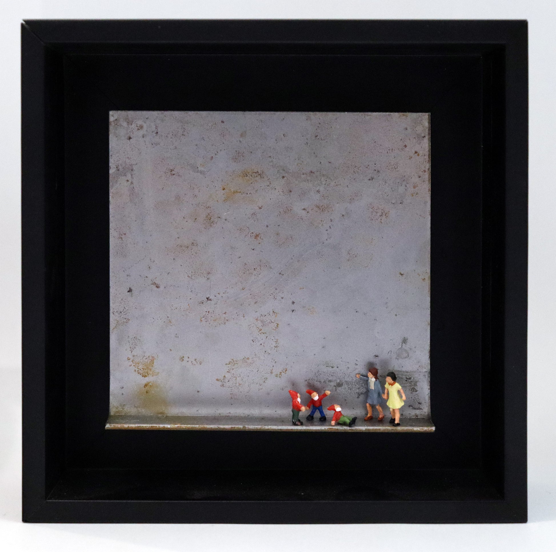 Original Objekt - Assemblage von Katrin Schramm, Titel „Zwergengeflüster.“ – Metallwinkel mit Miniatur-Figuren: Zwei Frauen/Mädchen stehen am rechten Rand des Winkels. Neben ihnen eine Gruppe aus drei Zwergen mit roten Mützen. Einer sitzt und schaut zu ihnen hoch, die beiden anderen stehen dahinter. Dahinter das Metall des Winkels mit Struktur, als Hintergrund. Objektcollage im schwarzen Rahmen, erhältlich bei Galerie Waldbach - What The Artist Made