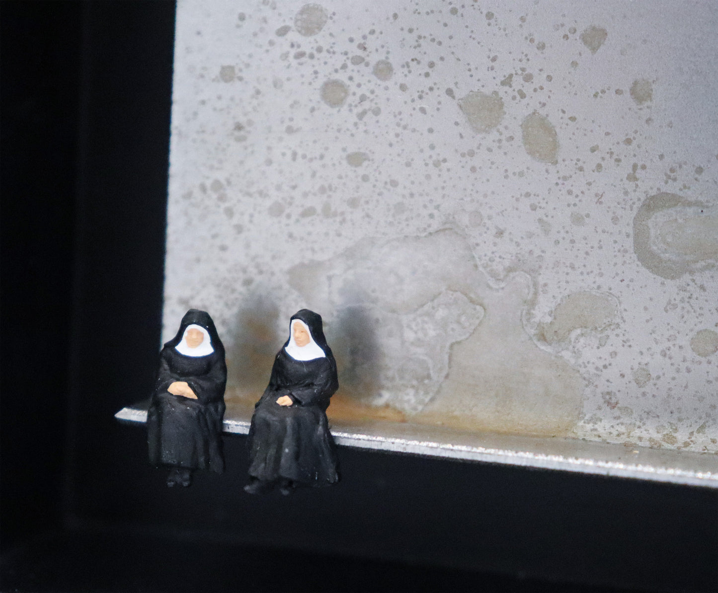 Original Objekt - Assemblage von Katrin Schramm, Titel „Ach Gott...“ – Metallwinkel mit Miniatur-Figuren, Detailansicht. Dahinter das Metall des Winkels mit Struktur, als Hintergrund. Objektcollage im schwarzen Rahmen, erhältlich bei Galerie Waldbach - What The Artist Made