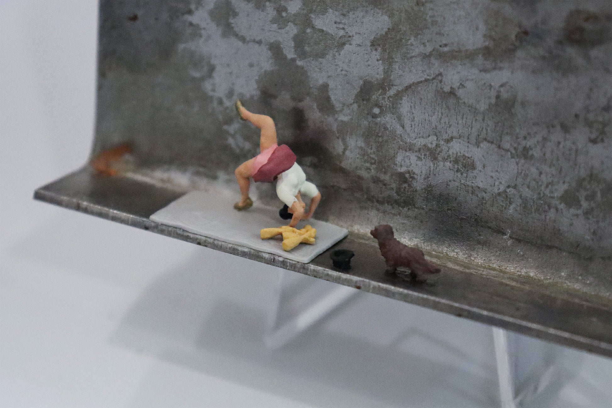 Original Objekt - Assemblage von Katrin Schramm, Titel „Weil sie s kann.“ – Metallwinkel mit Miniatur-Figuren, Detailansicht. Dahinter das Metall des Winkels mit Struktur, als Hintergrund. Objektcollage, erhältlich bei Galerie Waldbach - What The Artist Made