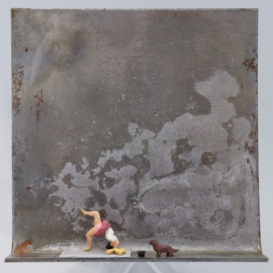 Original Objekt - Assemblage von Katrin Schramm, Titel „Weil sie s kann.“ – Metallwinkel mit Miniatur-Figuren: Eine Frau macht eine Brücke auf einer Yogamatte. Vor ihr ein handtuch und ein Hut, sowie ein kleiner brauner Hund, der sie anschaut. Dahinter das Metall des Winkels mit Struktur, als Hintergrund. Objektcollage, erhältlich bei Galerie Waldbach - What The Artist Made