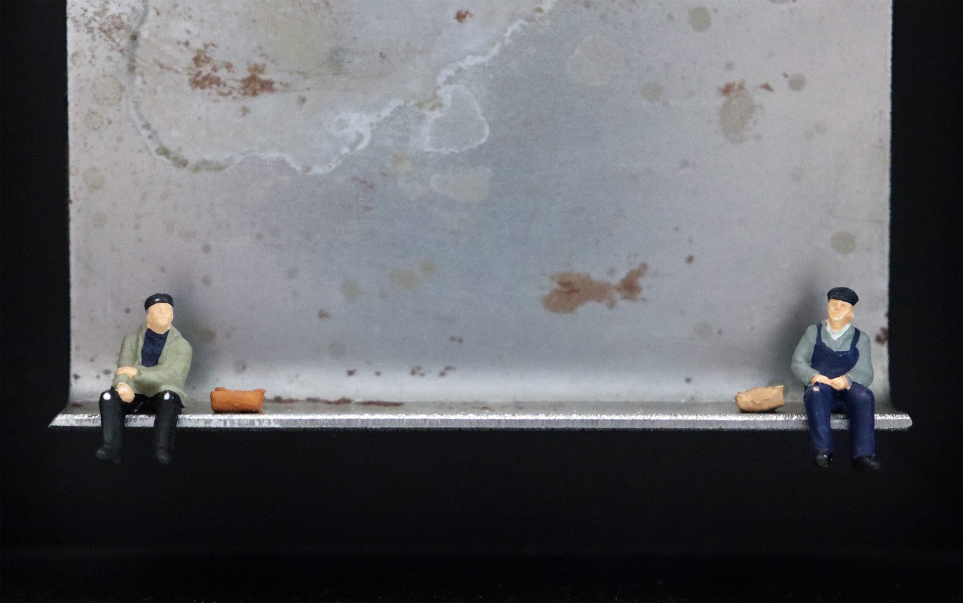 Original Objekt - Assemblage von Katrin Schramm, Titel „Moin       Moin“ – Metallwinkel mit Miniatur-Figuren, Detailansicht. Dahinter das Metall des Winkels mit Struktur, als Hintergrund. Objektcollage im schwarzen Rahmen, erhältlich bei Galerie Waldbach - What The Artist Made